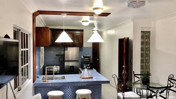 A kitchen with a blue tiled backsplash, stainless steel appliances, and a glass dining table with chairs. - Close to the ocean—the perfect spot to explore Puerto Plata on foot (Puerto Plata)