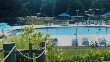 A swimming pool with lounge chairs and umbrellas, surrounded by a fence and greenery.