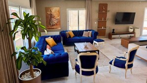 Uma sala de estar com um sofá azul, uma mesa de centro e uma televisão na parede.