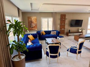 Ein Wohnzimmer mit blauem Sofagarnitur, einem Couchtisch und einem an der Wand befestigten Fernseher.