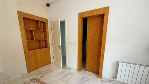 Um quarto com soalho em mosaico, guarda-roupa de madeira com prateleira embutida e radiador.
