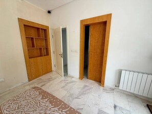 Ein Zimmer mit gefliestem Boden, einem Holzschrank mit integriertem Regal und einem Heizkörper.