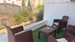 Uma varanda com móveis de vime, uma pequena mesa e vista para um prédio e árvores.