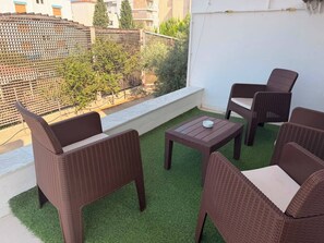 Ein Balkon mit Korbmöbeln, einem kleinen Tisch und Blick auf ein Gebäude und Bäume.