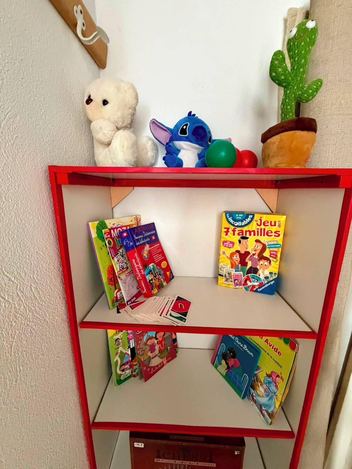A shelf with children's books, a stuffed toy, and a cactus.