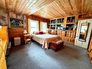 Una habitación con paneles de madera, una cama, un estante con trofeos y una puerta con espejo.