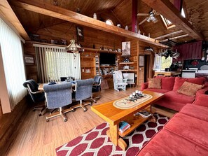 Een gezellig chaletinterieur met een eethoek, een rode bank en een houten plafond.