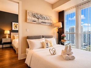 Una habitación de hotel con cama, mesita de noche, lámpara, un cuadro y vistas a la ciudad.