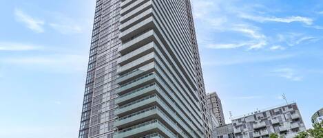 A tall, modern skyscraper with a grid-like facade, surrounded by urban buildings and a street with cars and pedestrians.