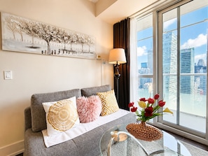 Ein modernes Wohnzimmer mit grauem Sofa, Zierkissen und Blick auf die Stadt, inklusive Wandlampe.