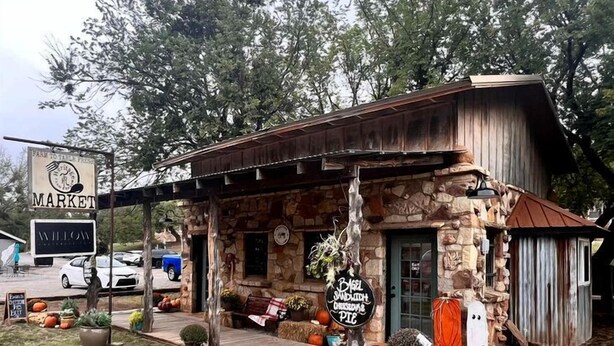 Un edificio rústico con fachada de piedra y un porche de madera, rodeado de árboles y calabazas.