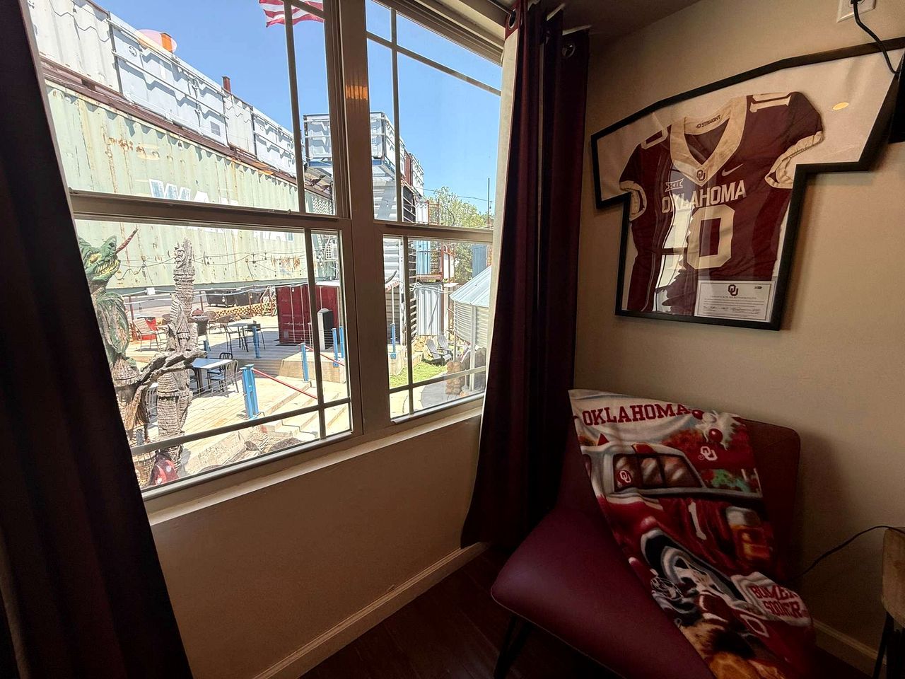 A room with a large window, a red chair, and a wall-mounted jersey.