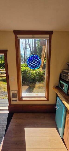 A kitchen with a large window, a microwave, and a small refrigerator. - Pacific Coral Cove - a cozy rainforest studio for two (Ucluelet)