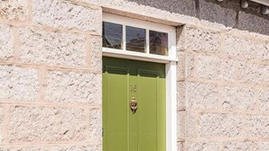 Un edificio de piedra con puerta verde, una ventana encima de la puerta y un pequeño porche.