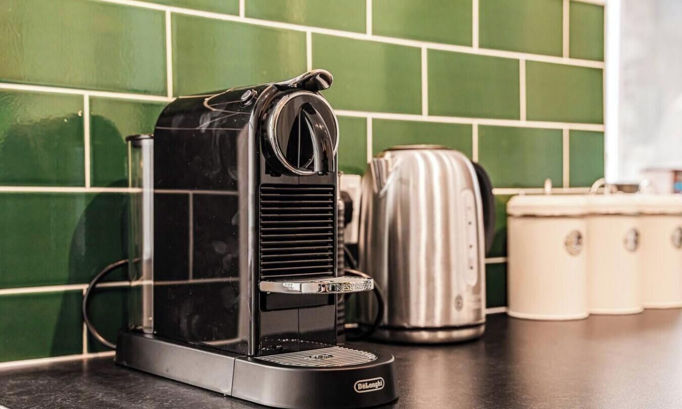 Une machine à café posée sur un plan de travail de cuisine, avec un dosseret de carreaux verts.