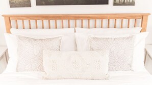 Una cama con cabecera de madera, ropa de cama blanca y almohadas estampadas.