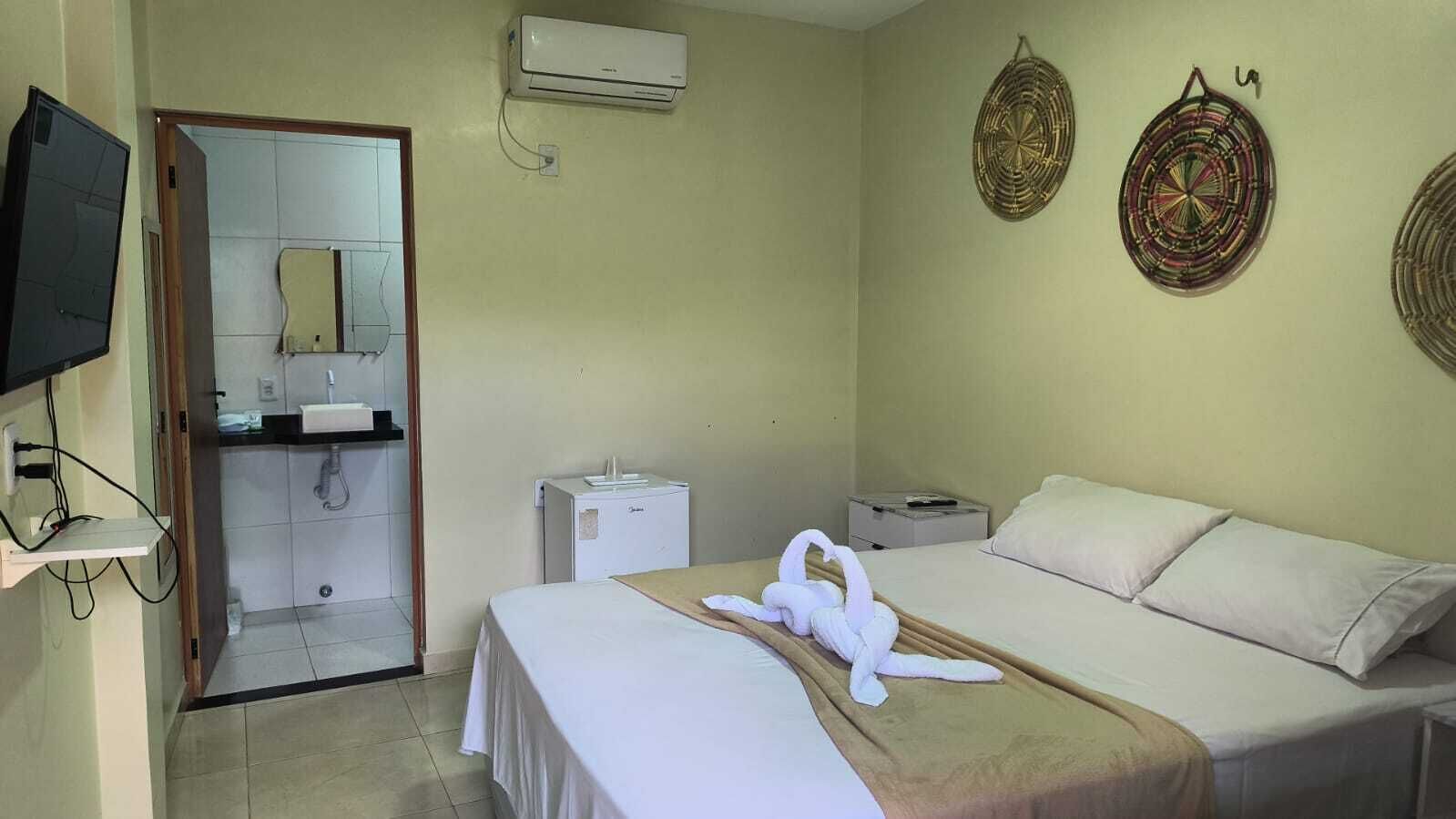Habitación de hotel con cama, televisión, minibar y baño visible a través de una puerta abierta.