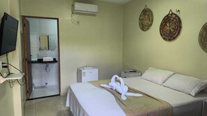 Habitación de hotel con cama, televisión, minibar y baño visible a través de una puerta abierta.