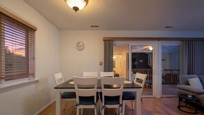 Een eethoek met een tafel en stoelen, een klok aan de muur en uitzicht op het landschap door een schuifdeur.