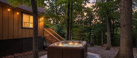 A hot tub in a forested area with a wooden building in the background.