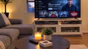 A living room with a TV displaying Netflix content, a remote control, a candle, and a stack of books on a coffee table.