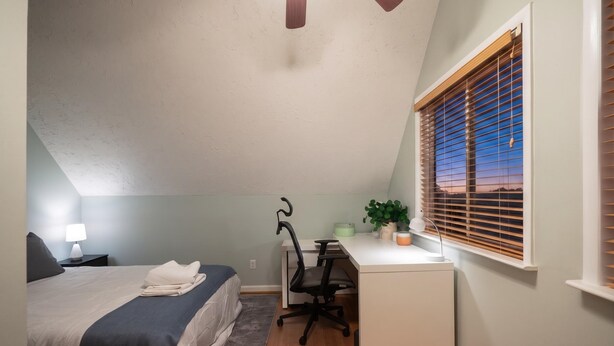 Een slaapkamer met een bed, bureau, stoel en een raam met zonwering.