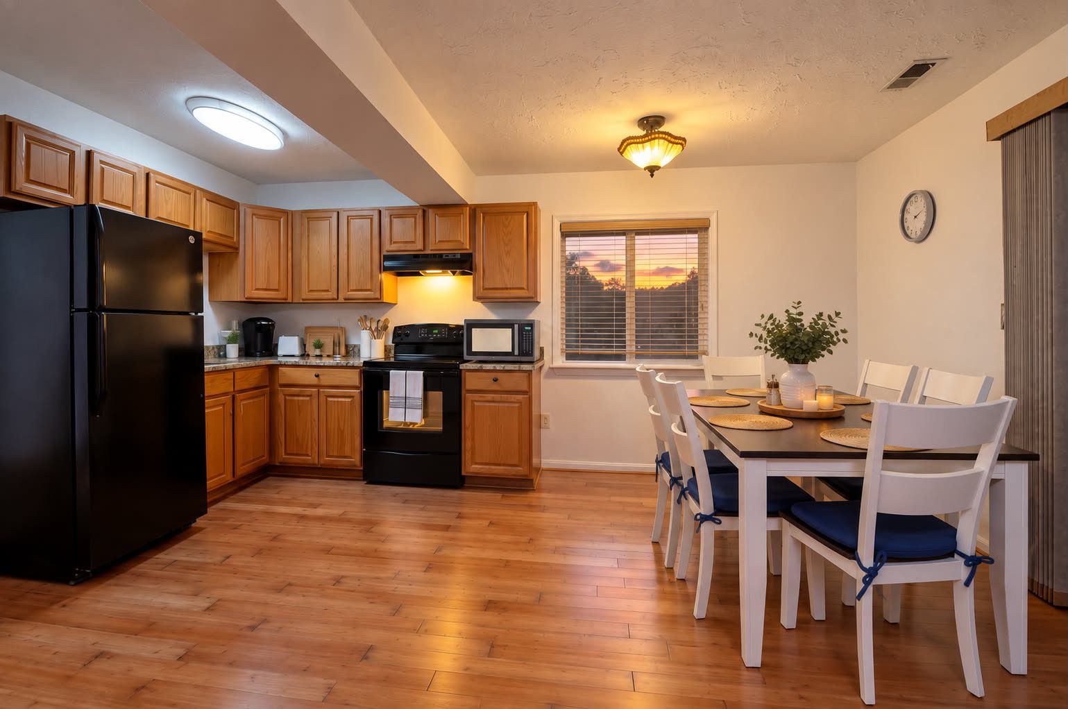 A kitchen with wooden cabinets, a black refrigerator, a stove, and a dining area with a table and chairs.