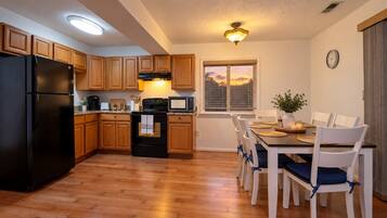 A kitchen with wooden cabinets, a black refrigerator, a stove, and a dining area with a table and chairs.