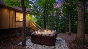 Een hottub in een bebost gebied, met een houten huis en een trap naar een terras.