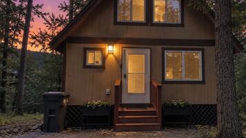 A wooden cabin with a front door, two windows, and a small porch with steps.