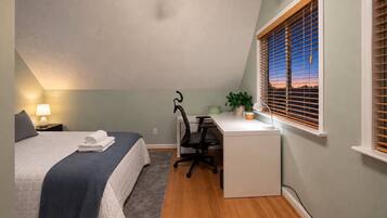 A bedroom with a bed, desk, chair, and a window with blinds.