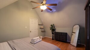 Een slaapkamer met een bed, een plafondventilator, een dressoir, een spiegel en een plant.