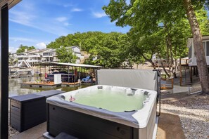 A hot tub with a covered seating area, a dock with boats, and a view of houses and trees. - Lakefront 7BR retreat: Hot Tub Game Room Fire Pit (Lake Ozark)