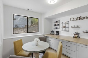 Una cocina moderna con una mesa redonda de comedor, sillas y un ventanal con vistas a una casa y árboles.
