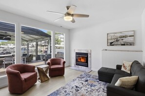 A modern living room with a fireplace, a ceiling fan, and a view of a marina. - Lakefront Retreat: Hot Tub, Game Room, Fire Pit (Lake Ozark)