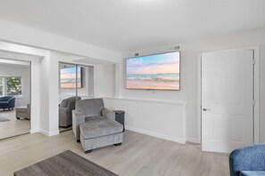 A modern living room with a grey sofa, a flat-screen TV mounted above it, and a door to the right. - Lakefront Retreat: Hot Tub, Game Room, Fire Pit (Lake Ozark)