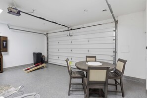 A garage with a table and chairs, a trash bin, and a ladder. - Lakefront Retreat: Hot Tub, Game Room, Fire Pit (Lake Ozark)