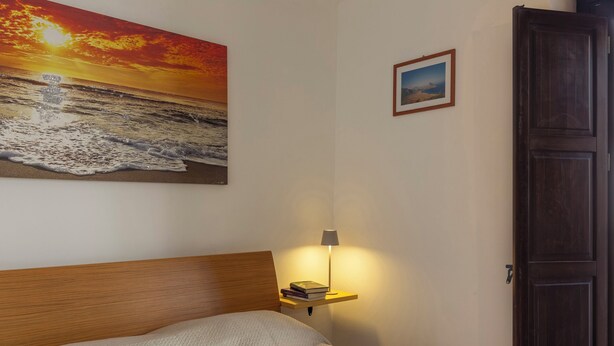 Et soveværelse med en seng, et sengebord med en lampe, et billede i ramme på væggen og en dør.