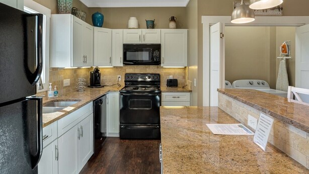 A modern kitchen with white cabinets, a black refrigerator, a microwave, a stove, and granite countertops. - The Fairview Hideaway (Fairview)