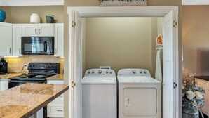 A compact kitchen with a stove, microwave, and a washing machine unit. - The Fairview Hideaway (Fairview)