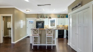 A modern kitchen with white cabinets, a central island with bar stools, pendant lighting, and a view of the outdoors through a window. - The Fairview Hideaway (Fairview)