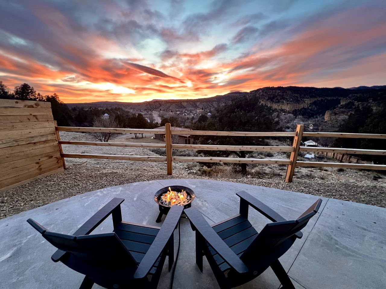 An outdoor seating area with a fire pit, wooden benches, and a view of a valley during sunset.