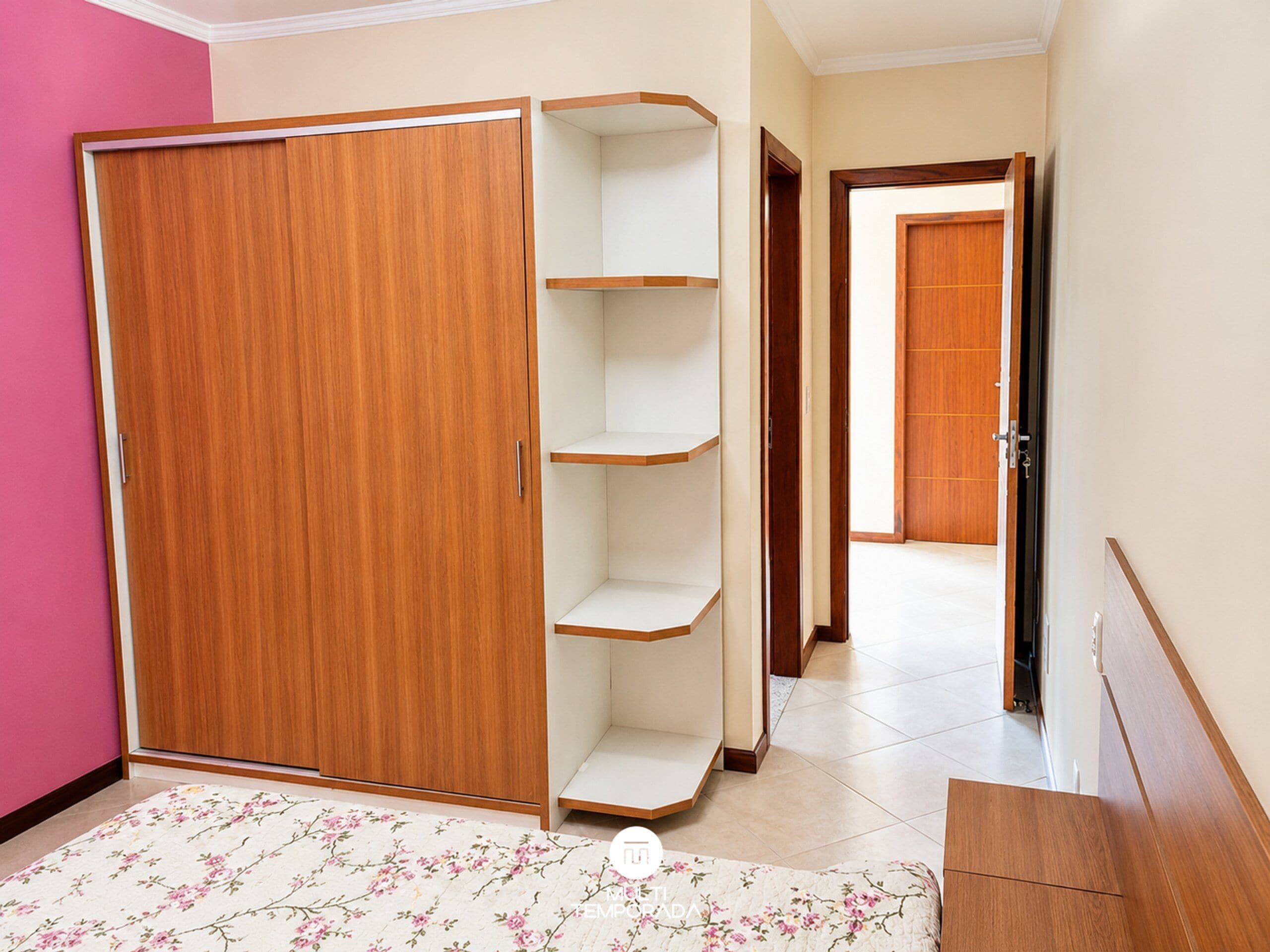 Een kamer met een houten garderobe, een wit wandrek en een vloerkleed met bloemenmotief.