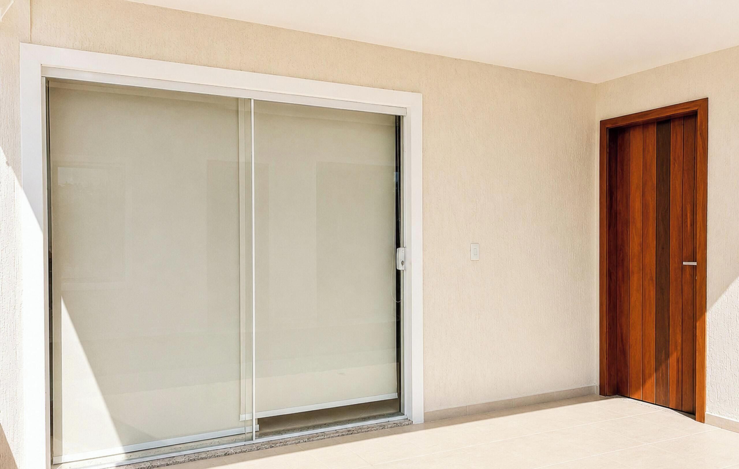 Una habitación con una puerta corrediza de vidrio que da a un espacio exterior, una puerta de madera y piso de baldosas.