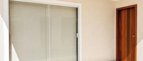 Una habitación con una puerta corrediza de vidrio que da a un espacio exterior, una puerta de madera y piso de baldosas.