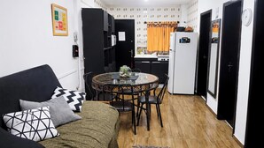 A compact living space with a sofa, a round dining table, and a kitchenette. - Ap Balcan 500mts da Praia - Balneario Camboriu /SC (Balneário Camboriú)