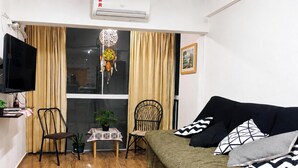 A compact living space with a sofa, a television, a small table with a plant, and a chair. - Ap Balcan 500mts da Praia - Balneario Camboriu /SC (Balneário Camboriú)