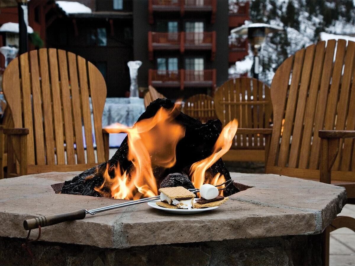 A stone table with a campfire, two wooden chairs, and a plate with s'mores.