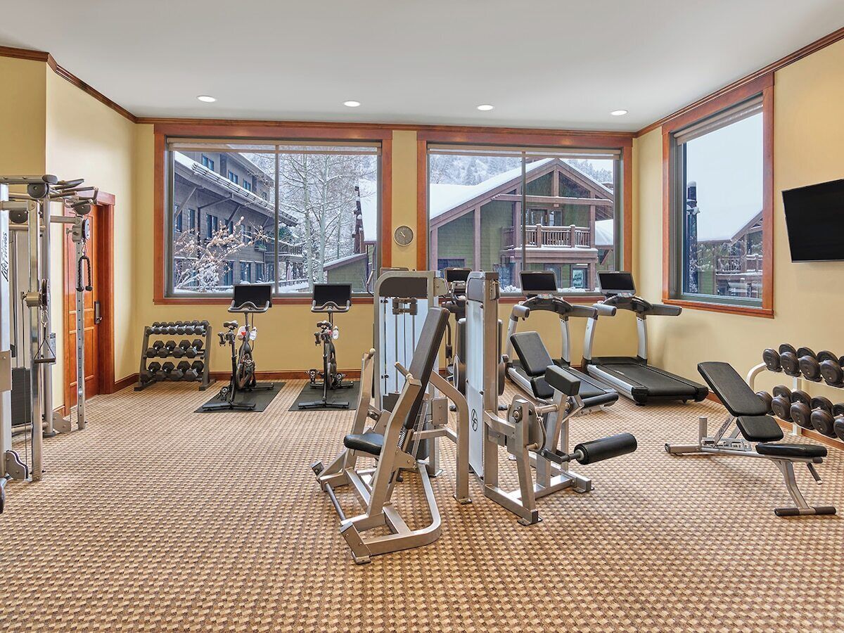 A gym with various exercise equipment, large windows, and a view of a building with snow outside.