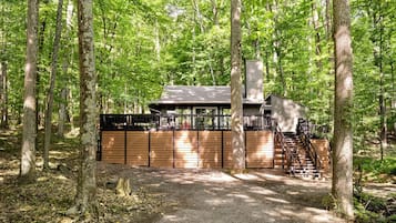 Une cabane dotée d’une terrasse en bois, d’une cheminée et d’un escalier menant à l’étage supérieur.